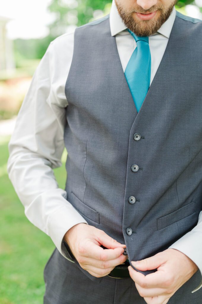 The groom buttoning his vest to get ready for his wedding day. 