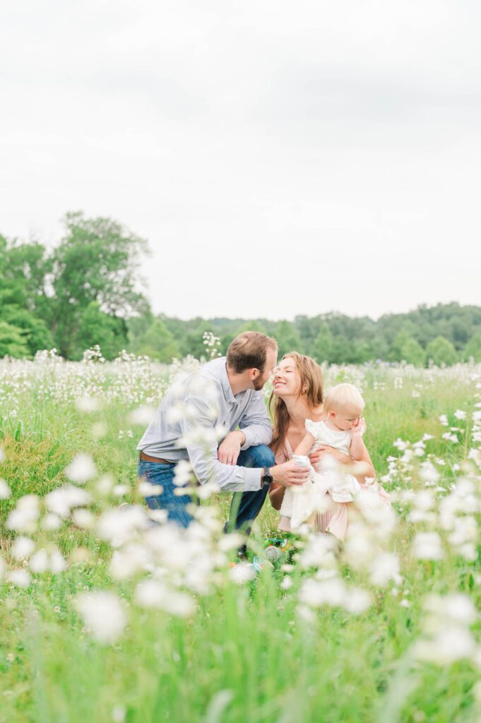 Mom and dad kiss while baby looks at the wildflowers during a Louisville family photo session