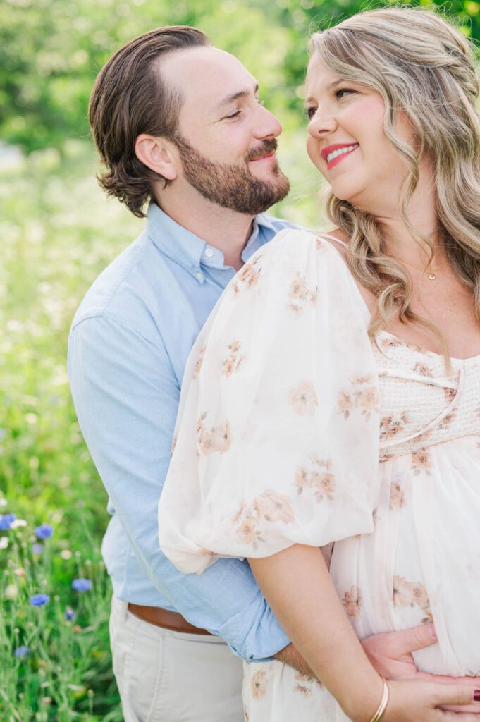 Couple stands together in wildflower field for their maternity photo session at Beckley Creek Park in Louisville