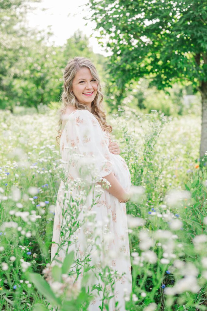 Expectant mother stands in wildflower field for maternity photo session at Beckley Creek Park in Louisville