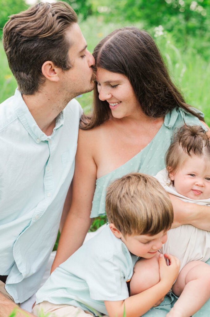 Dad gives mom a forehead kiss while brother hugs his sister for their photo session in Louisville, KY