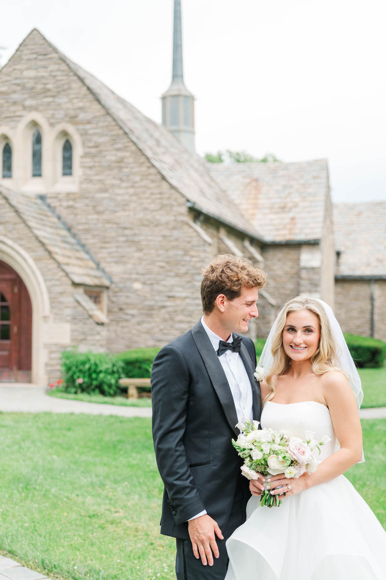wedding couple poses for portraits in front of the chapel before their ceremony