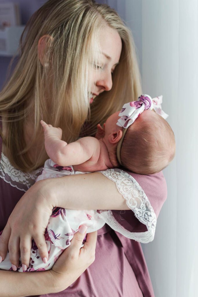 Mom smiles while holding baby girl during in-home newborn photography session in Lexington, KY
