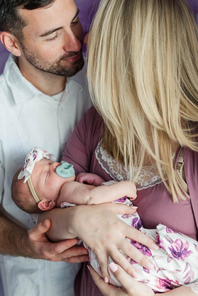 New parents smile while holding their baby girl during their in-home newborn photography session in Lexington, KY