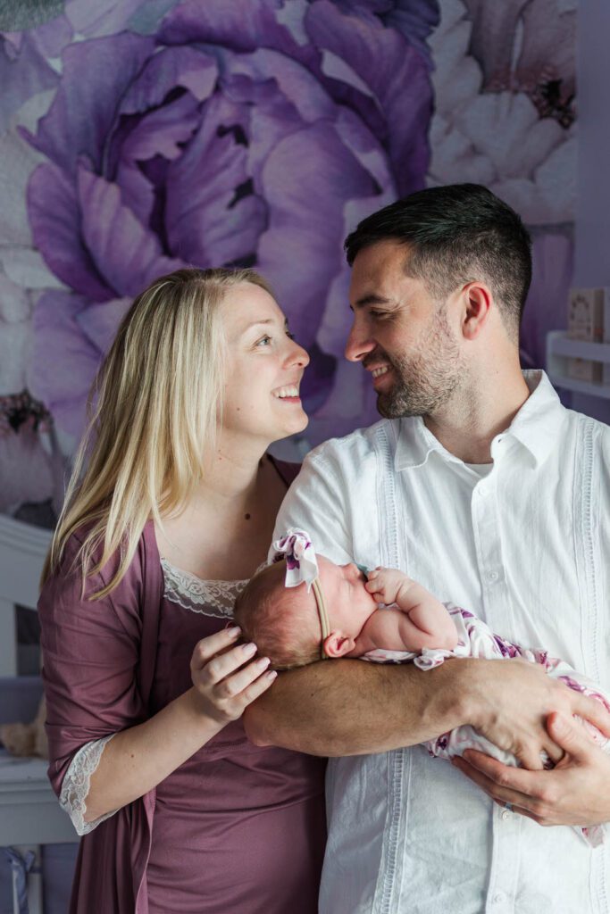 New parents smile while holding their baby girl during their in-home newborn photography session in Lexington, KY
