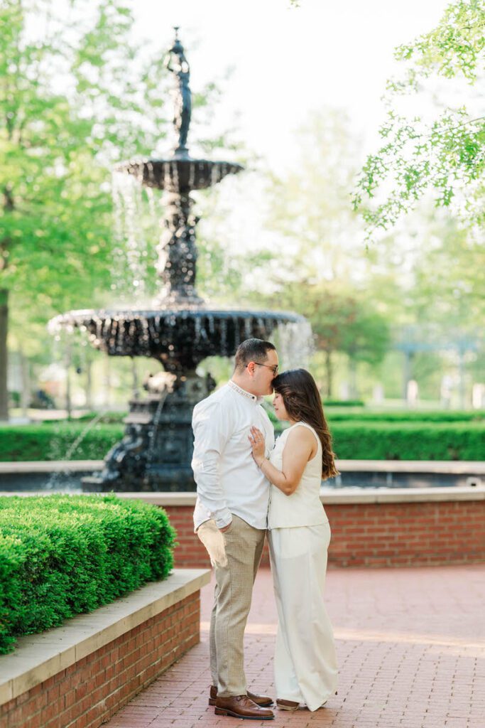 Couple embraces in front of the fountain for their engagement session in Norton Commons