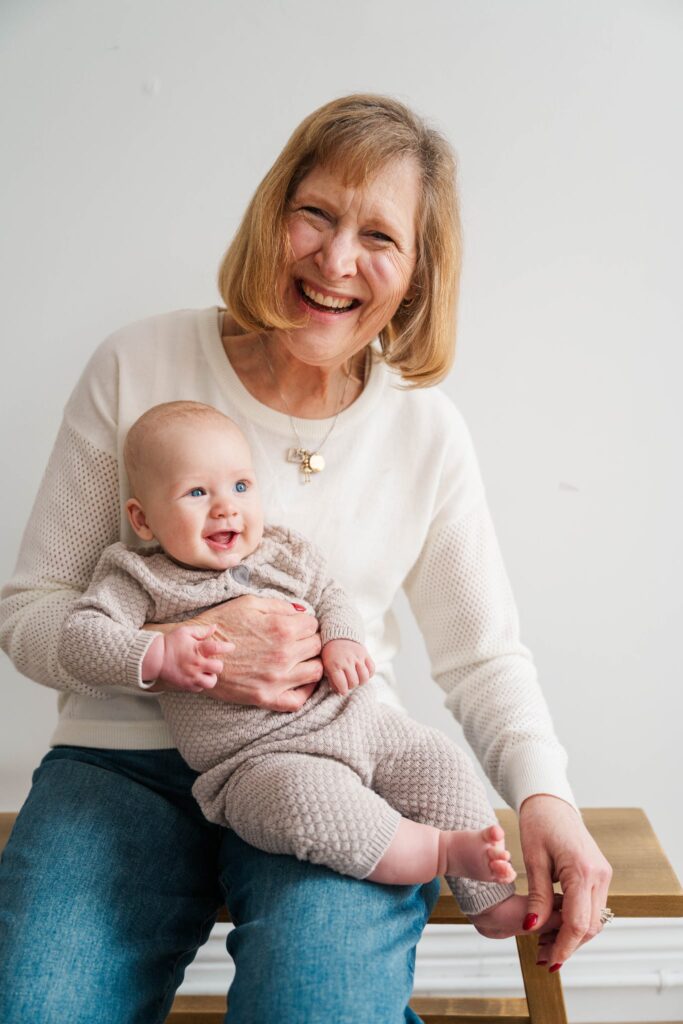 A grandmother smiles while holding her grandson. Louisville Motherhood Photographer Photos by Michelle Bordenkircher Photography