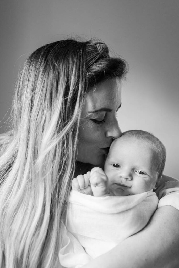 Mom kisses newborn baby, caught by Louisville photographer Michelle Bordenkircher during their in-home session.
