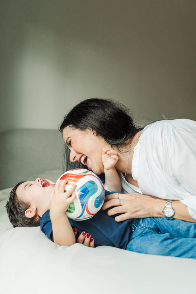Mom and son play in bed, caught by Louisville photographer Michelle Bordenkircher during their in-home maternity session.