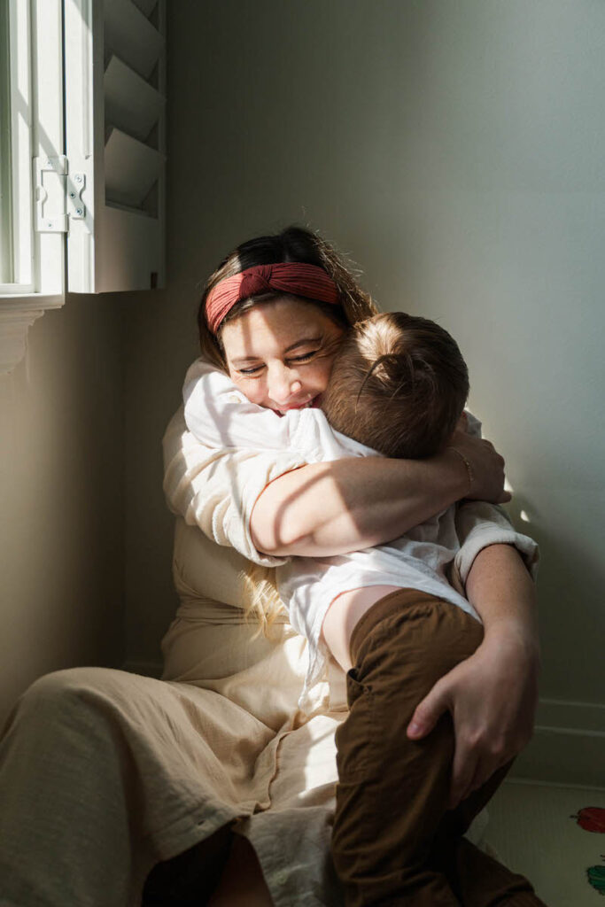 Mom and son hug in beautiful light in their Louisville living room.