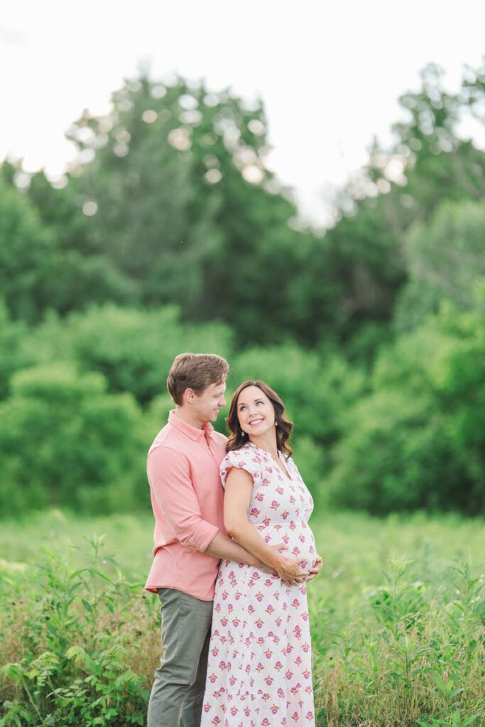 Expecting parents smile at each other in Beckley Creek Park