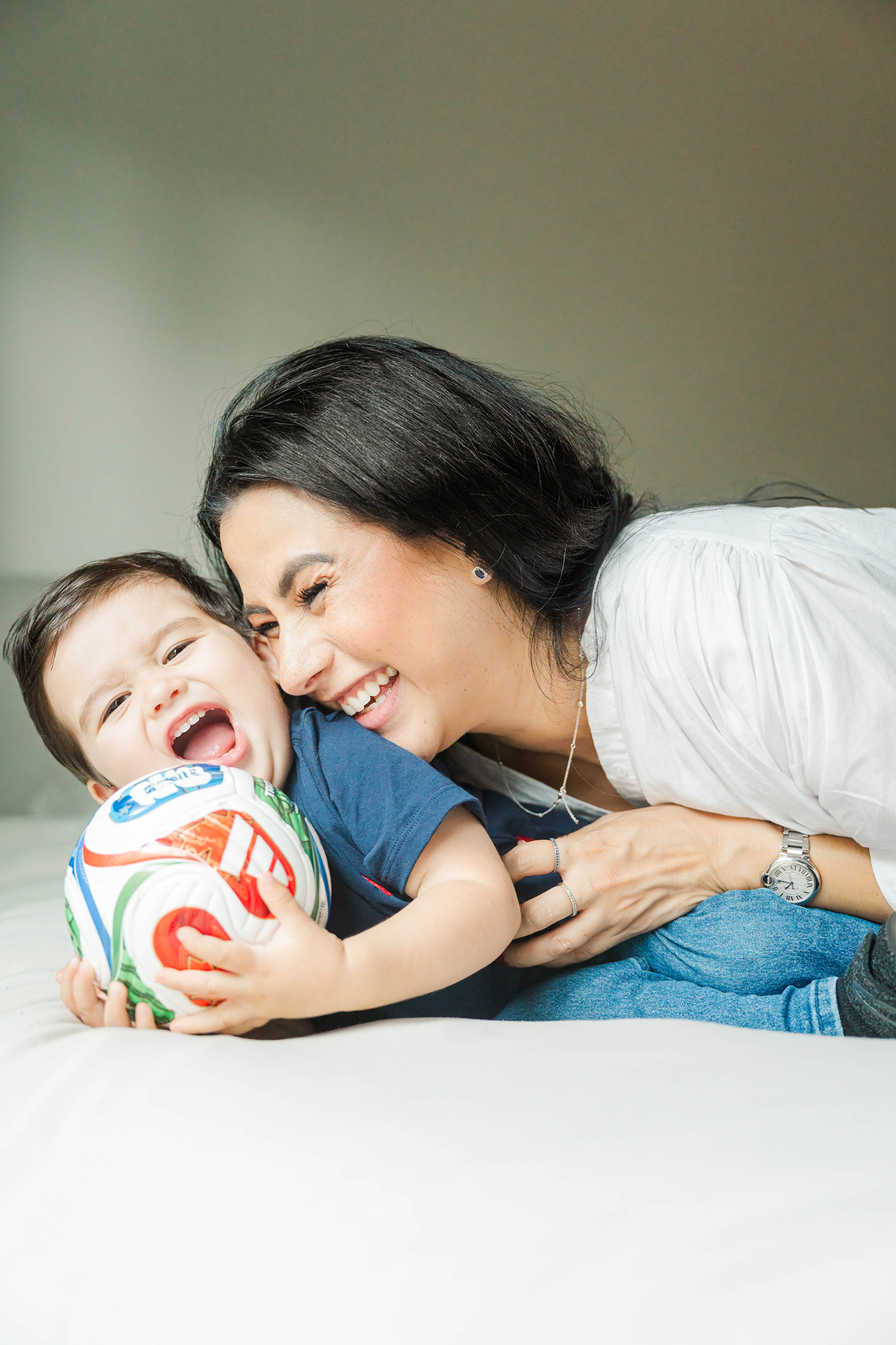Mom laughing with her toddler son holding a soccer ball on the bed taken by Louisville Family Photographer