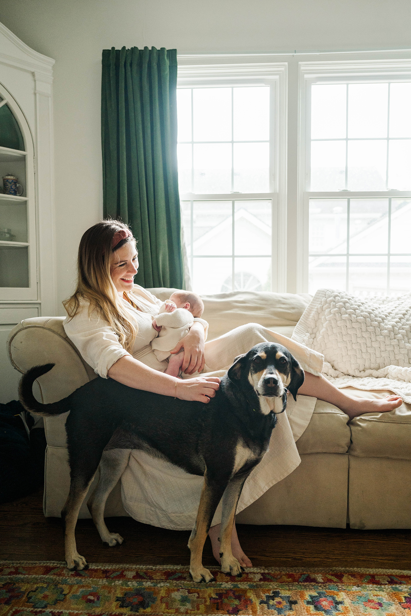 Mom nursing her newborn on the couch while the family dog stands watch, a relaxed in-home session by a Louisville Newborn Photographer