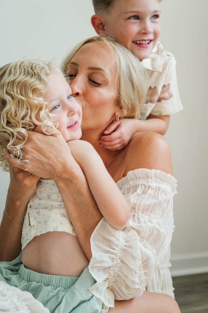 Expecting mom kisses her daughter while her son gives her a hug during her Louisville in-home maternity session.