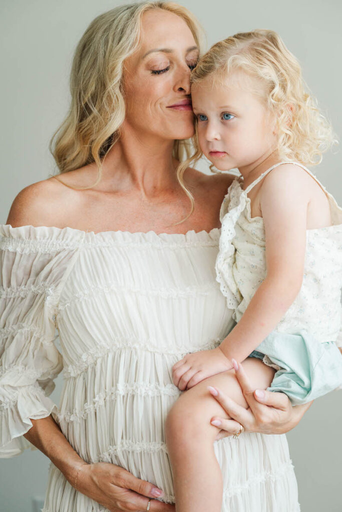 Mom snuggles her daughter while holding her pregnant belly.