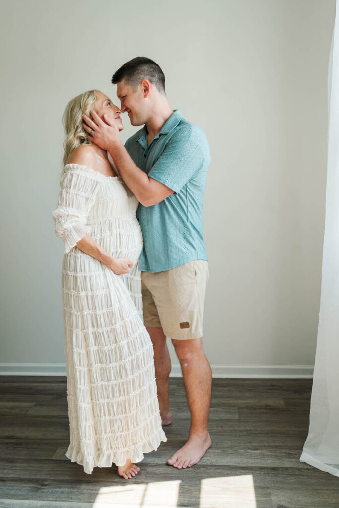 Expecting mom and dad snuggle together in beautiful in-home light during their maternity session.