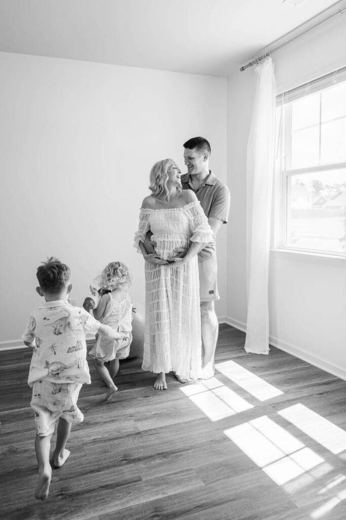 Expecting mom and dad smile at each other while their kids run around them during their Louisville in-home maternity session.