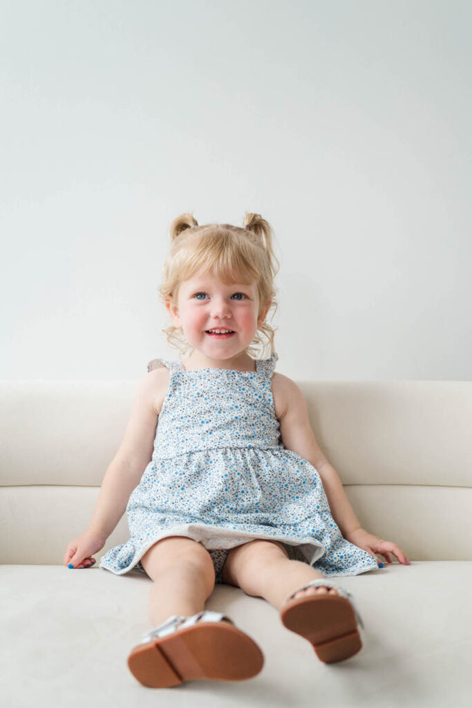 Two year old girl sits on the couch smiling at the camera during her Louisville mini session.