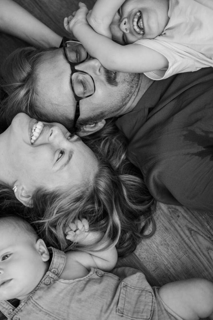 Mom, dad, and sons lay on floor together and play during their in-home family photos.