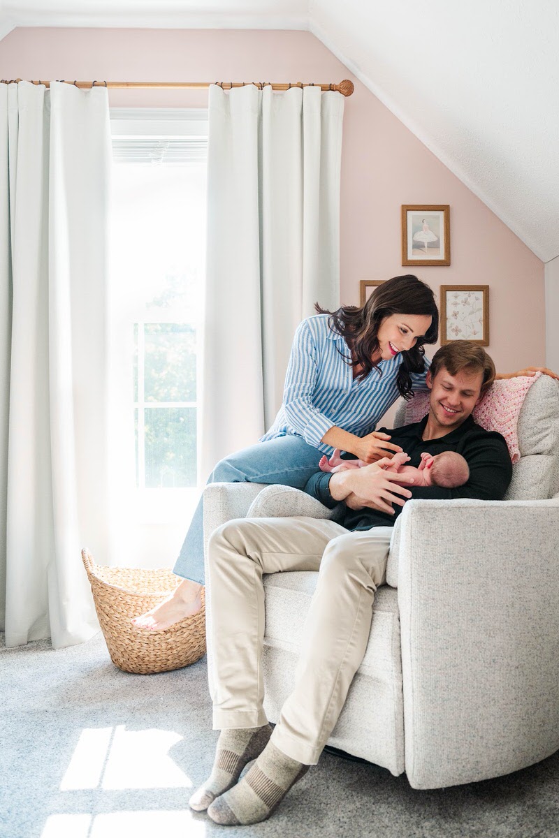 A new mom and dad smile down at their newborn baby girl in the nursery during their Louisville in-home newborn session.