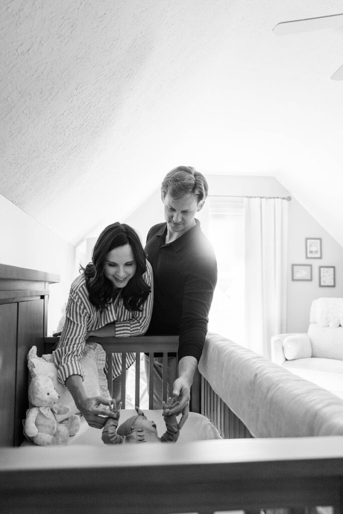 Mom and dad smile down at their new baby girl in her crib during their Louisville in-home newborn session.