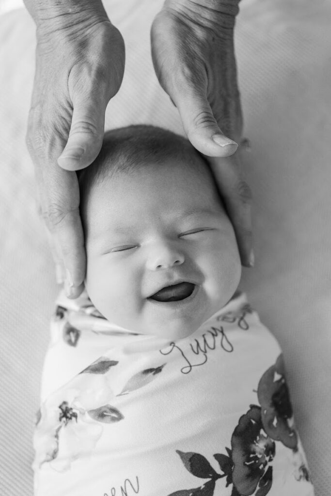Newborn baby girl smiles as her mom puts her hands on her head during her Louisville in-home newborn session.