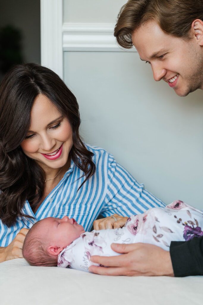 New parents smile down at their newborn baby girl during their in-home session.