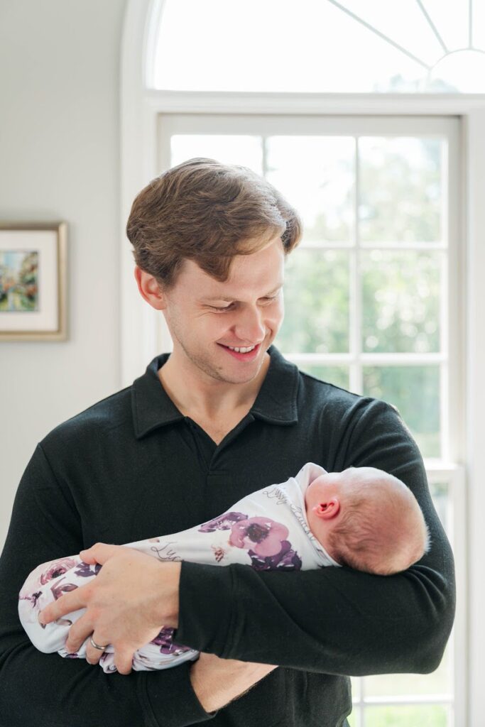 New dad smiles down at his baby girl during her in-home newborn session.