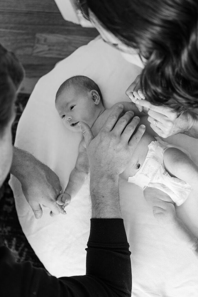 New parents smile down at their newborn baby girl during their in-home session.