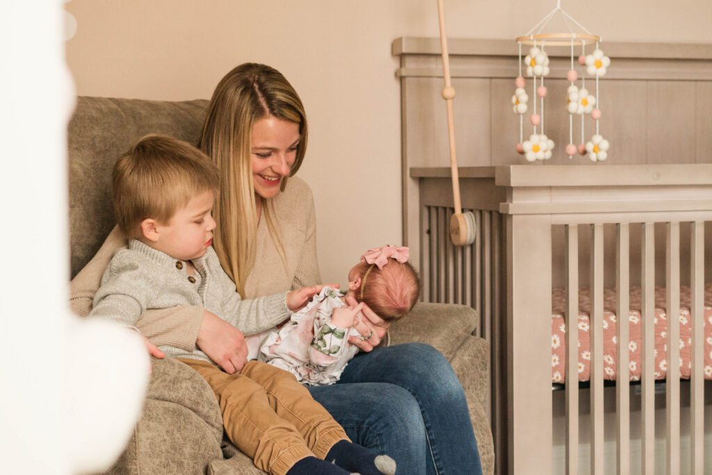 Mother holds newborn with older sibling in nursery