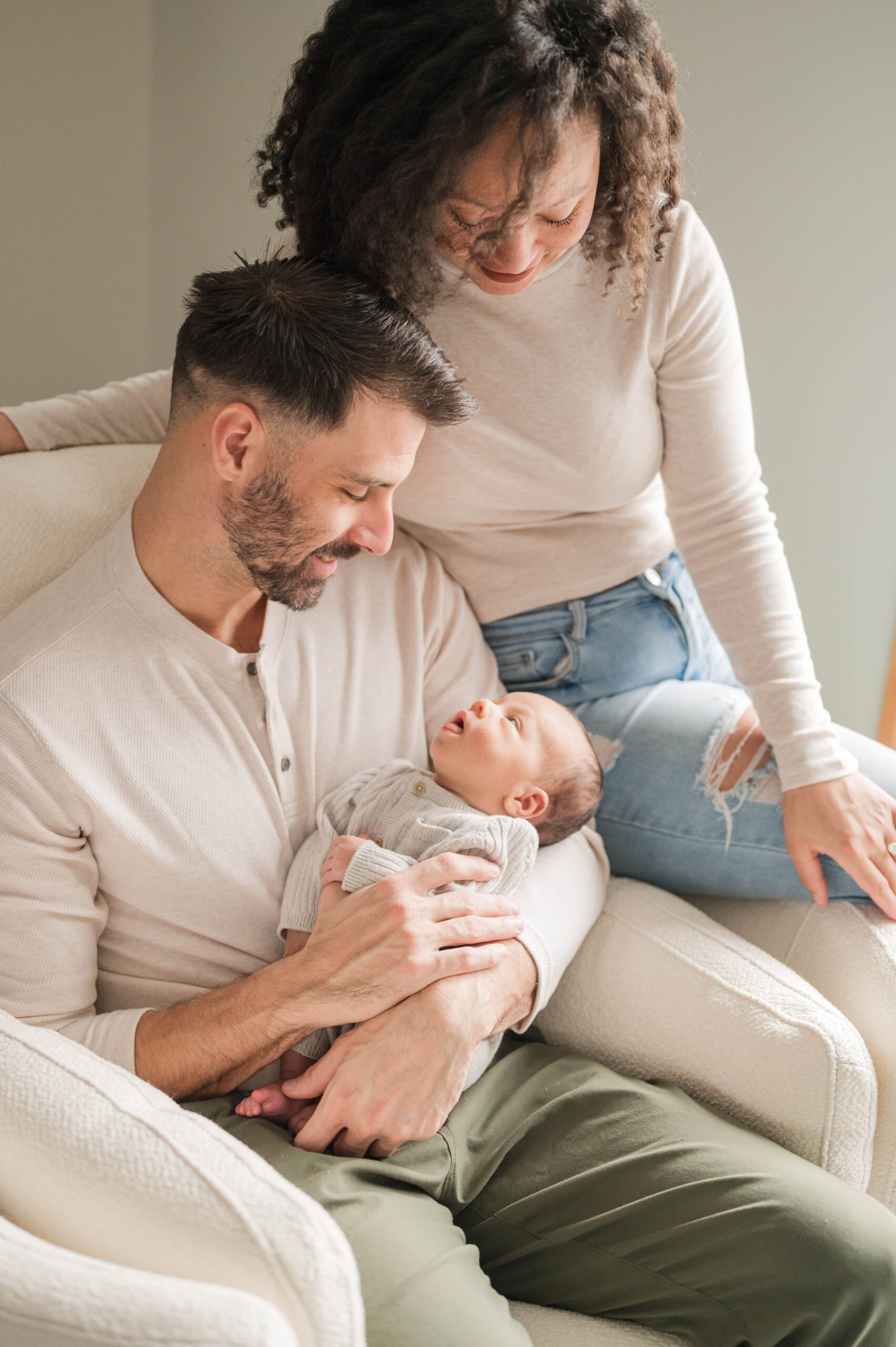 Mom and dad snuggle together to hold newborn baby in rocking chair