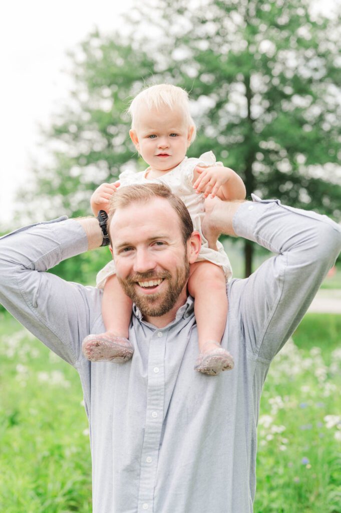 Dad smiles with his daughter on his shoulders