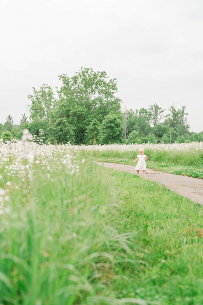 Baby girl walks on a path surrounded by wildflowers