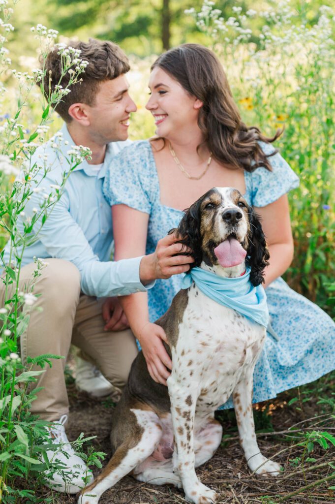 Couple sits together with their dog in a field of wildflowers at Beckley Creek Park for their Louisville engagement session.