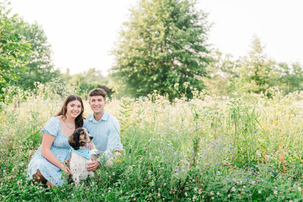 Couple sits together with their dog in a field of wildflowers at Beckley Creek Park for their Louisville engagement session.