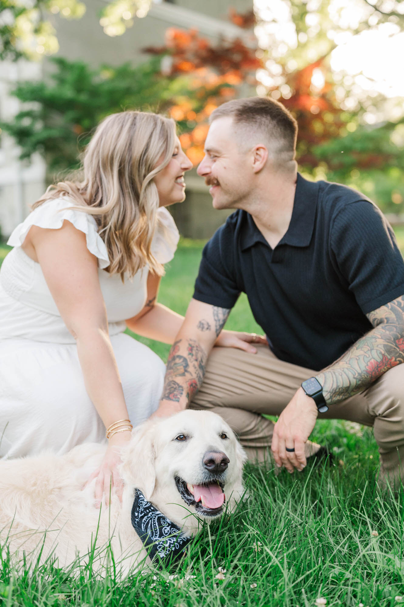 Couple smile at each other with their dog smiling at the camera in the foreground