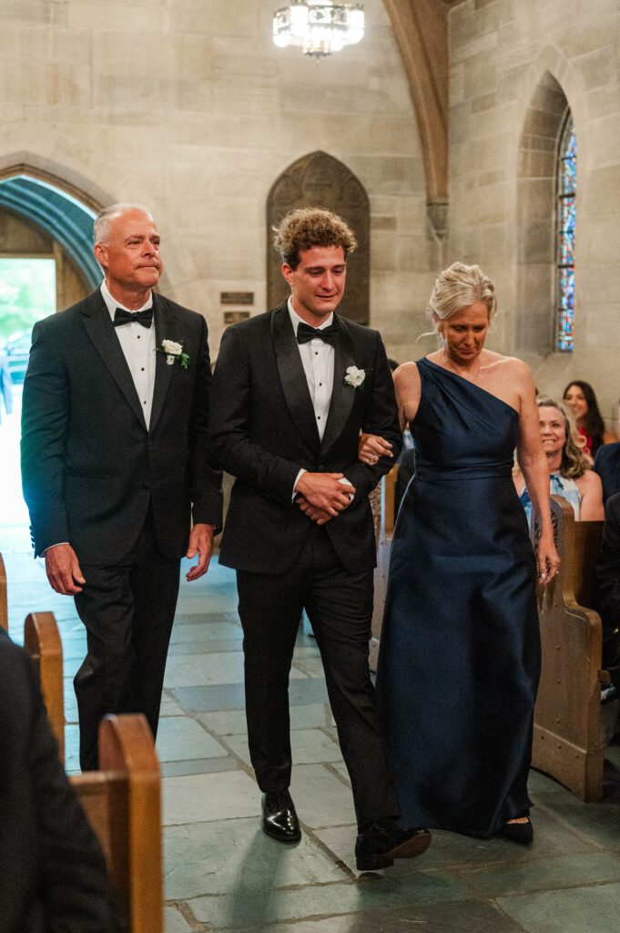 Groom walks down the aisle with his mom and dad before the wedding ceremony