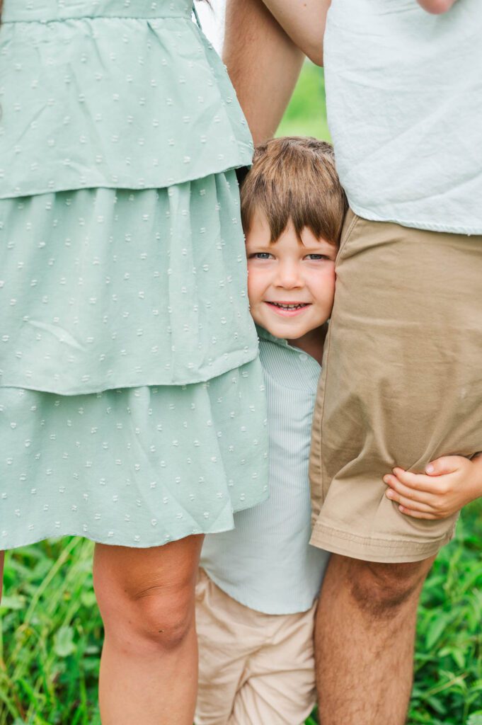 Three year old hugs mom and dad's legs during their photo session in Beckley Creek Park in Louisville, KY