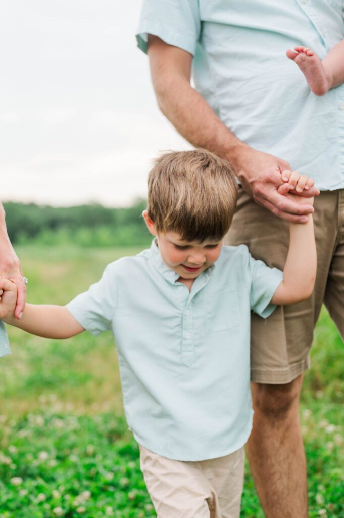 Three year old holds mom and dad's hands as they walk through a wildflower field in Beckley Creek Park in Louisville