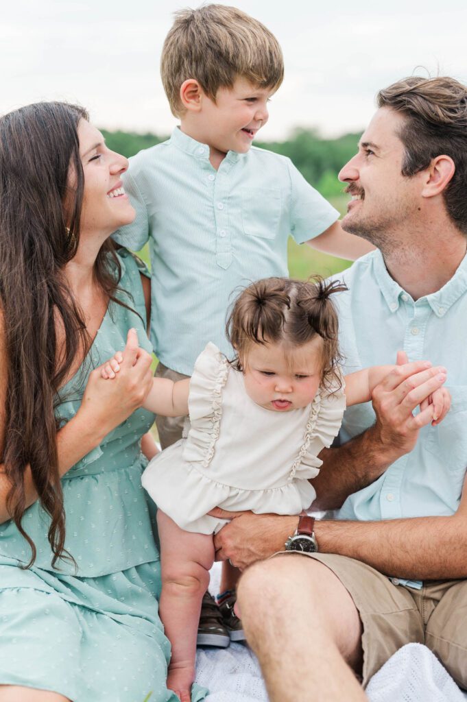 Family looks at each other smiling during their photo session in Beckley Creek Park in Louisville, KY