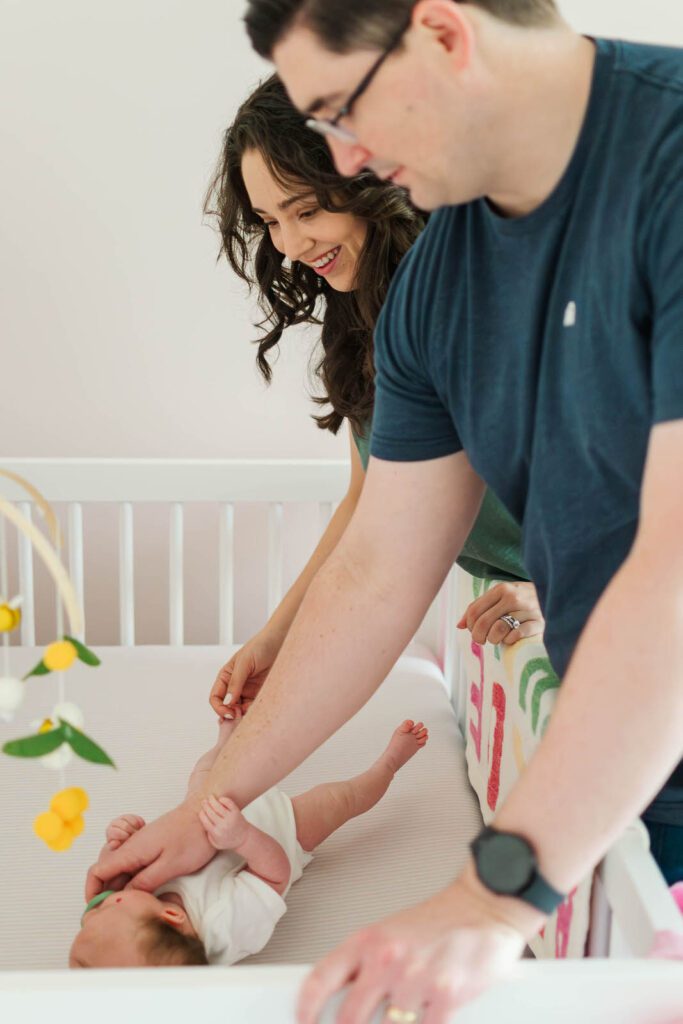 New parents stand at their newborn daughter's crib for their Louisville newborn photography session.