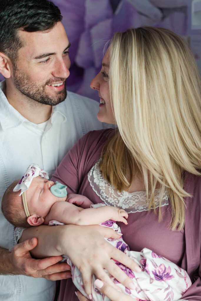 New parents smile at each other while holding their baby girl during their in-home newborn photography session in Lexington, KY