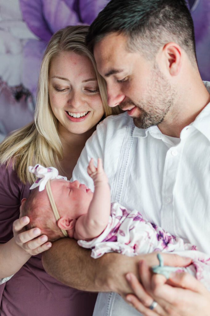 New parents smile while holding their baby girl during their in-home newborn photography session in Lexington, KY