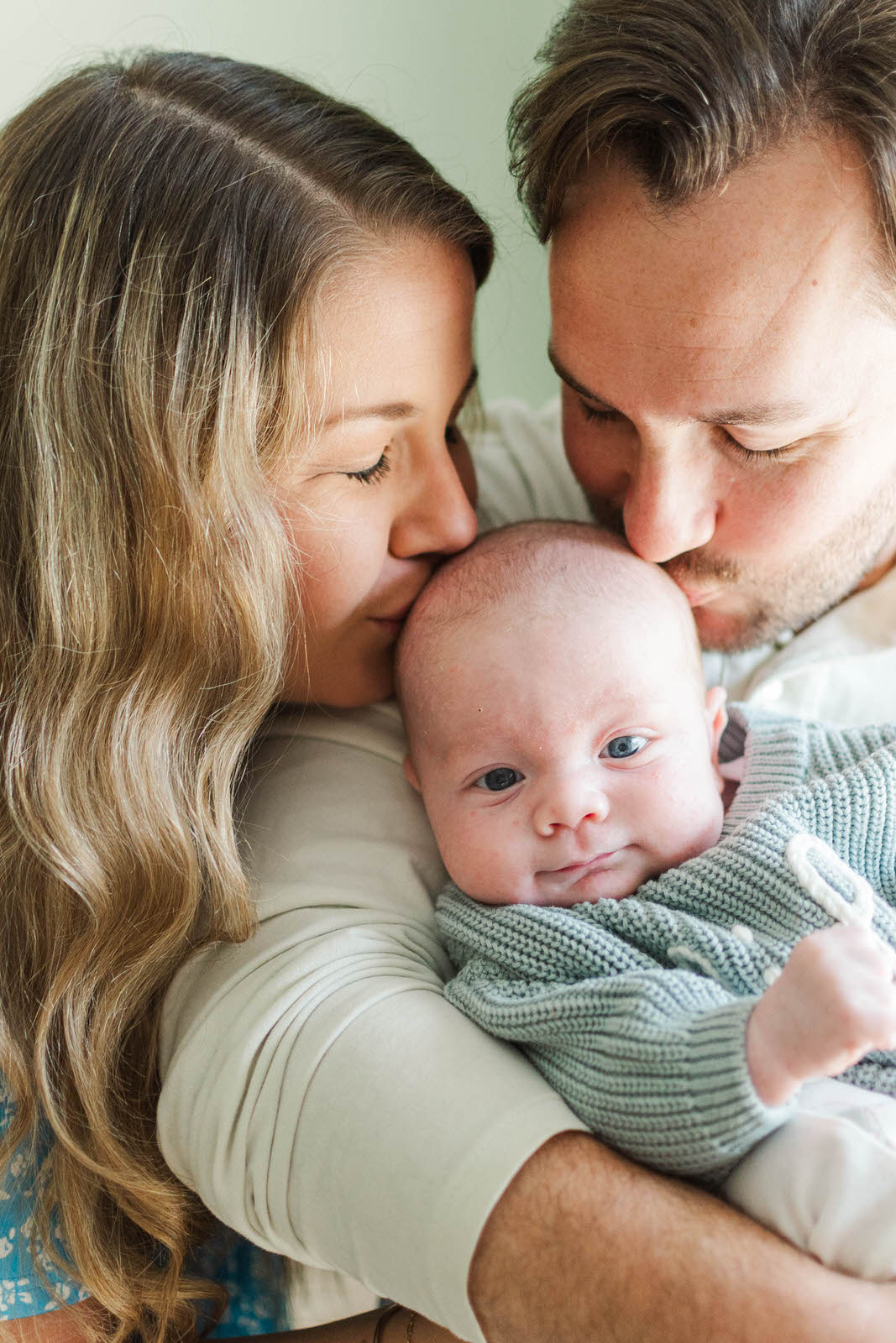 New mom and dad kiss their newborn baby during their in-home newborn session in Louisville, KY