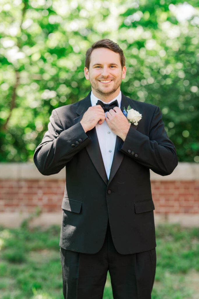 Groom straightening his bow tie on his wedding day