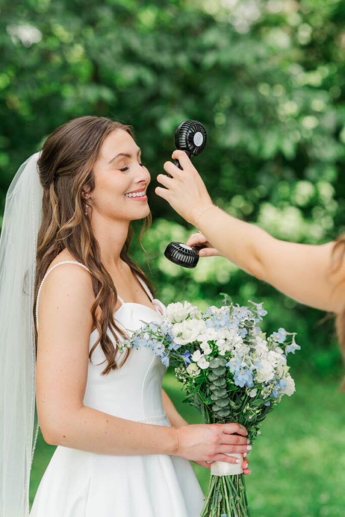 Bridesmaids use a fan to cool off the bride at her Gheens Foundation Lodge wedding