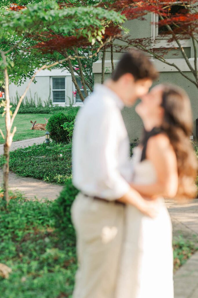 Couple smile at each other with deer in the background during their engagement session at Anchorage Trail in Louisville, KY