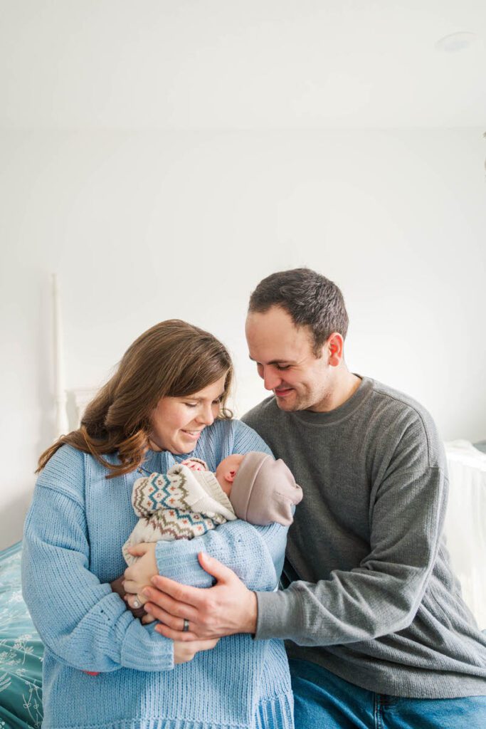 A mom and dad smile down at new baby during their in-home newborn session.