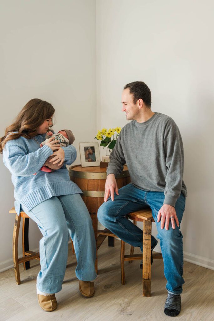 A mom and dad sit at a table, mom holding their newborn baby.