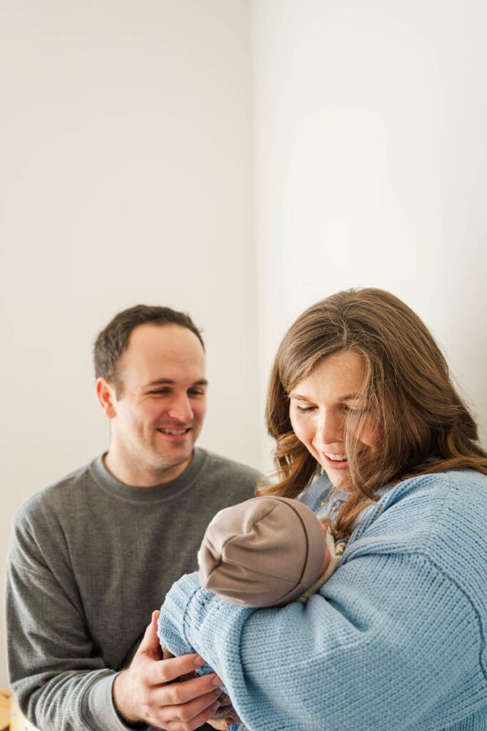 A new mom and dad smile at baby in mom's arms.